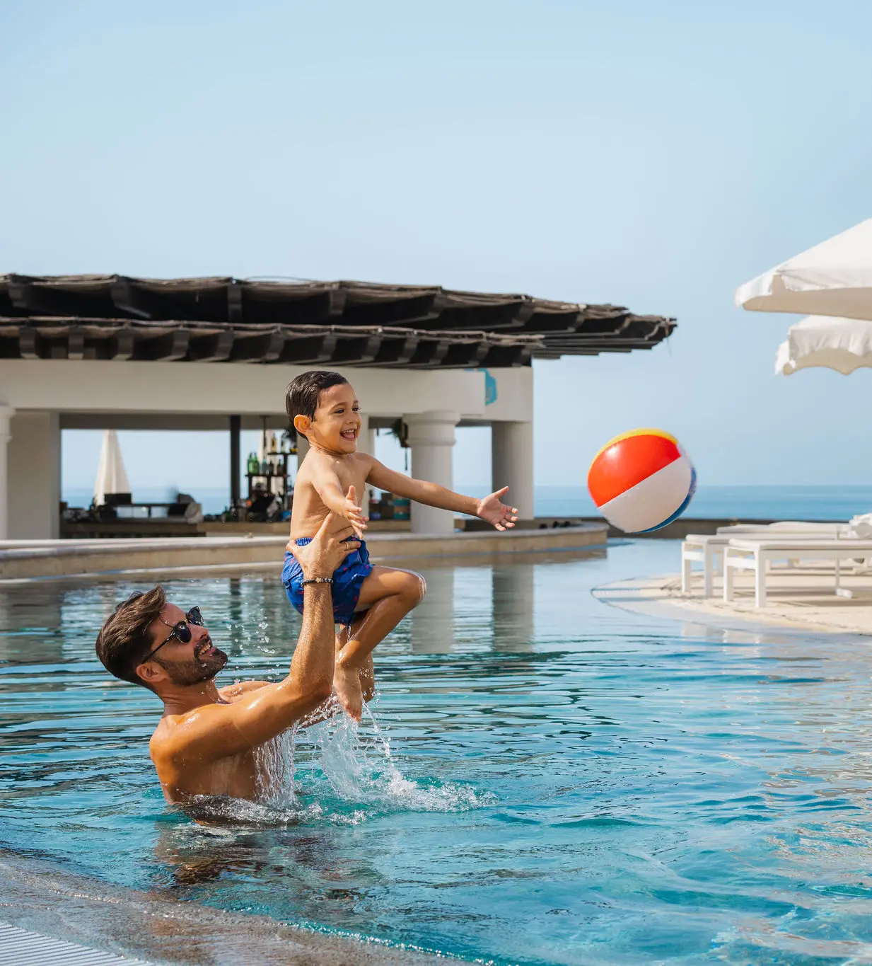 imagen de un hombre y un niño jugando con una pelota en la piscina