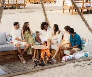 imagen de personas sentadas en san open cafe en la playa con fogata