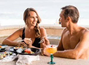 imagen de dos personas sosteniendo palillos y sentadas frente a un plato lleno de sushi