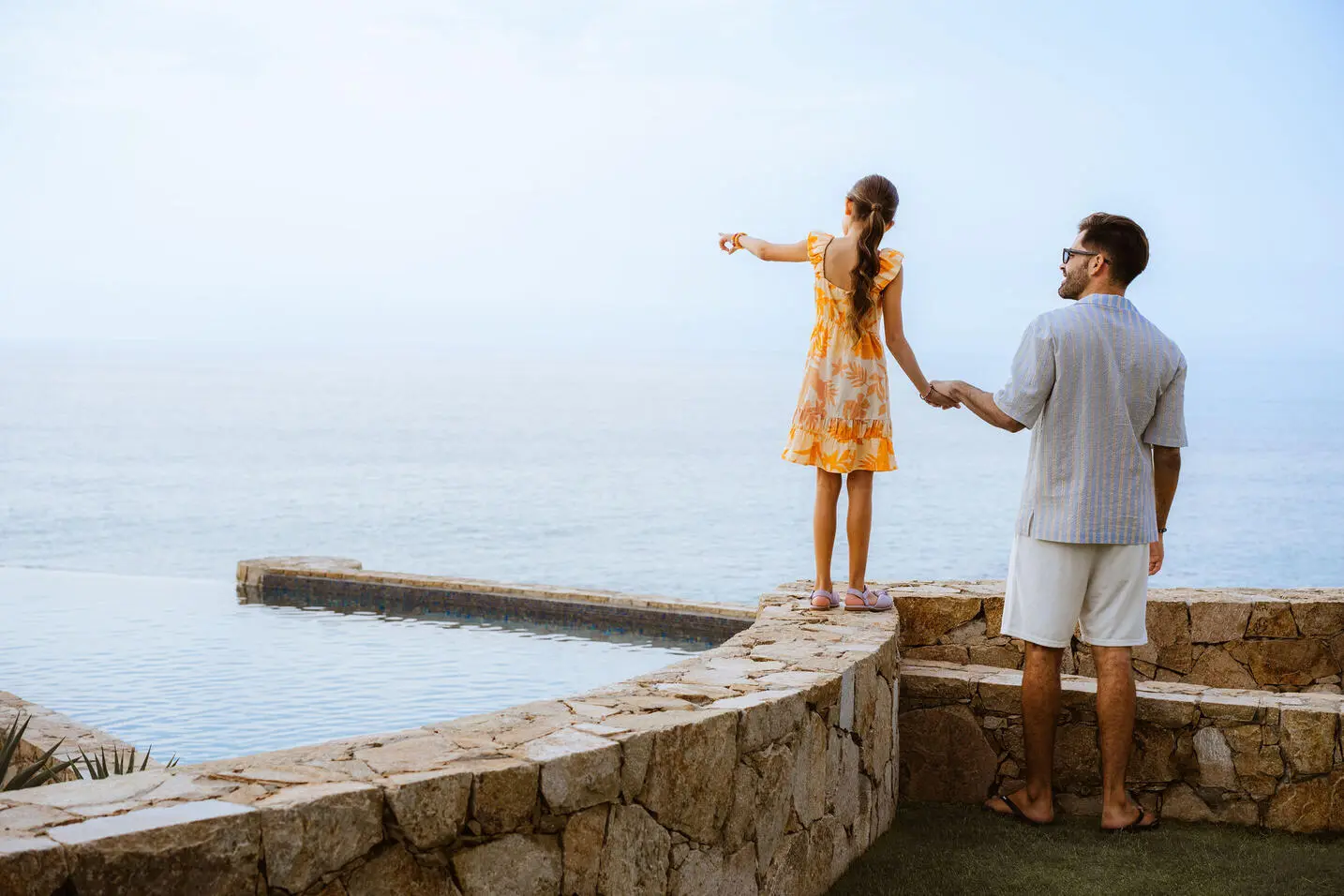 imagen de un hombre y una niña tomados de la mano mirando hacia el mar
