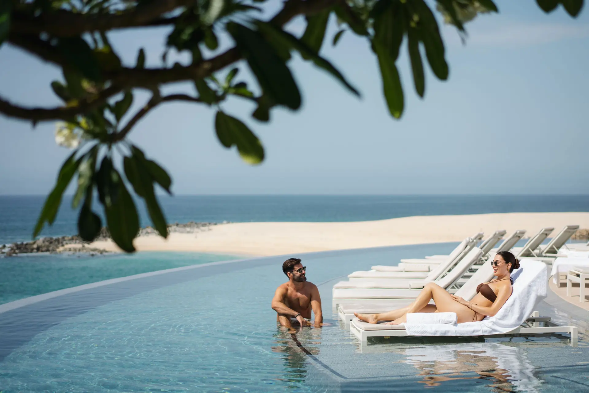 picture of a man and woman sitting near an infinity pool with sea view