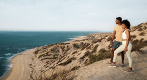imagen de dos personas de pie sobre una estructura similar a un domo de arena y mirando hacia el mar