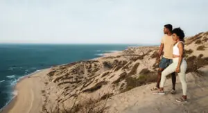 picture of two people standing on sand dome like structure and looking towards the sea