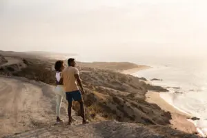picture of two people standing on sand dome like structure and looking towards the sea