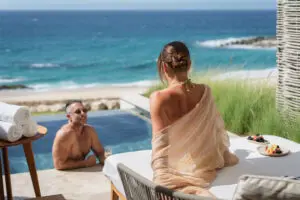 picture of a man in pool and women sitting on bench bed near the swimming pool