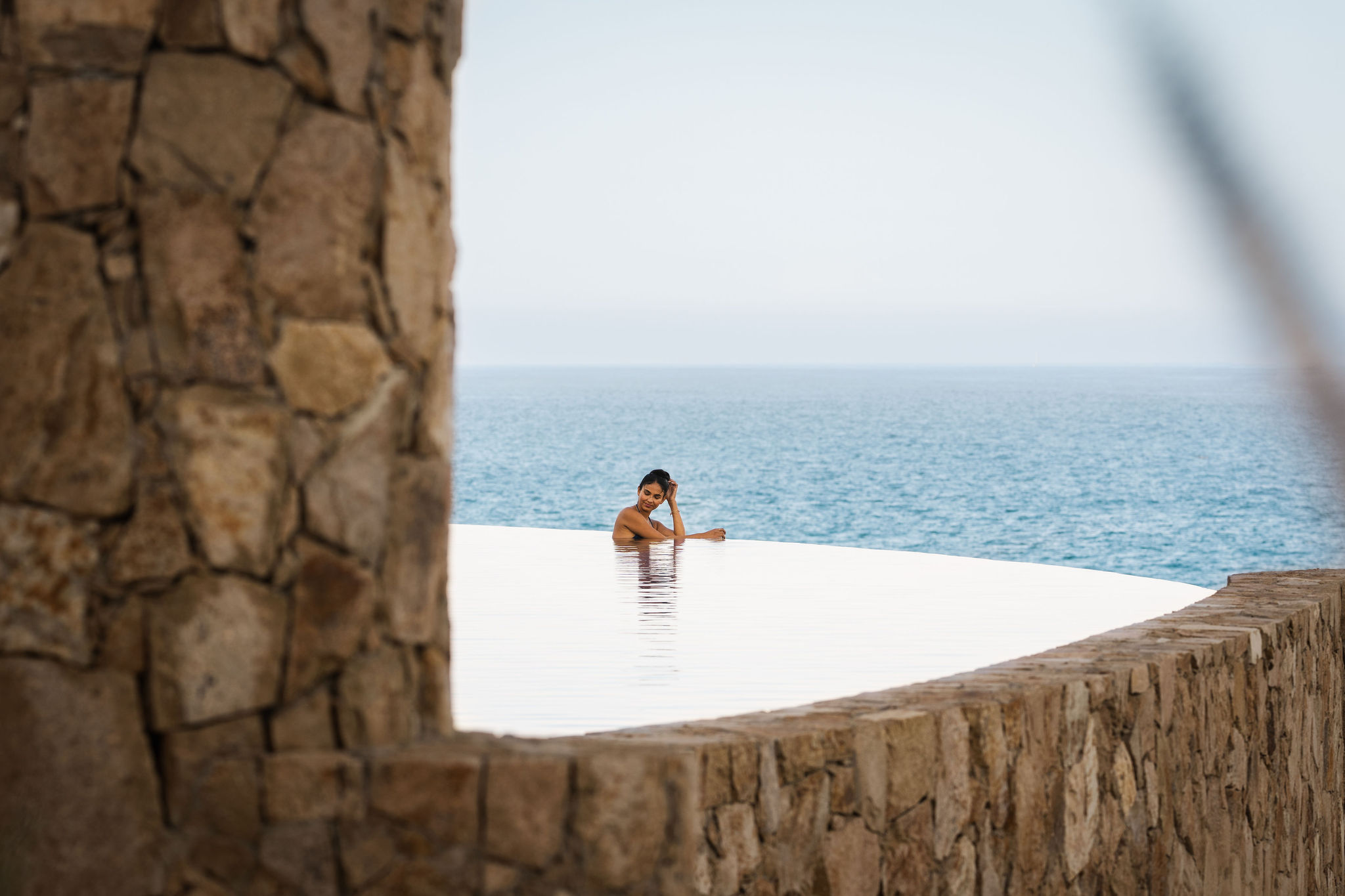 imagen de una mujer en una piscina infinita con vista al mar