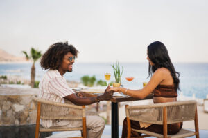 imagen de dos personas sentadas en un restaurante abierto tomados de la mano con vista al mar