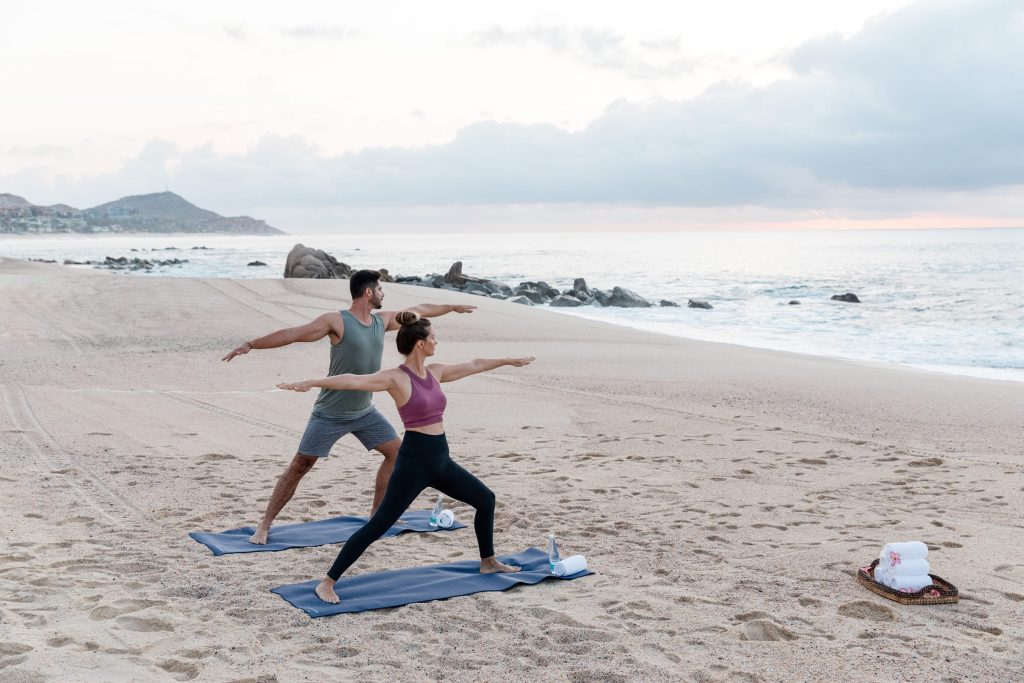 picture of two people doing yoga on beach with sea in front
