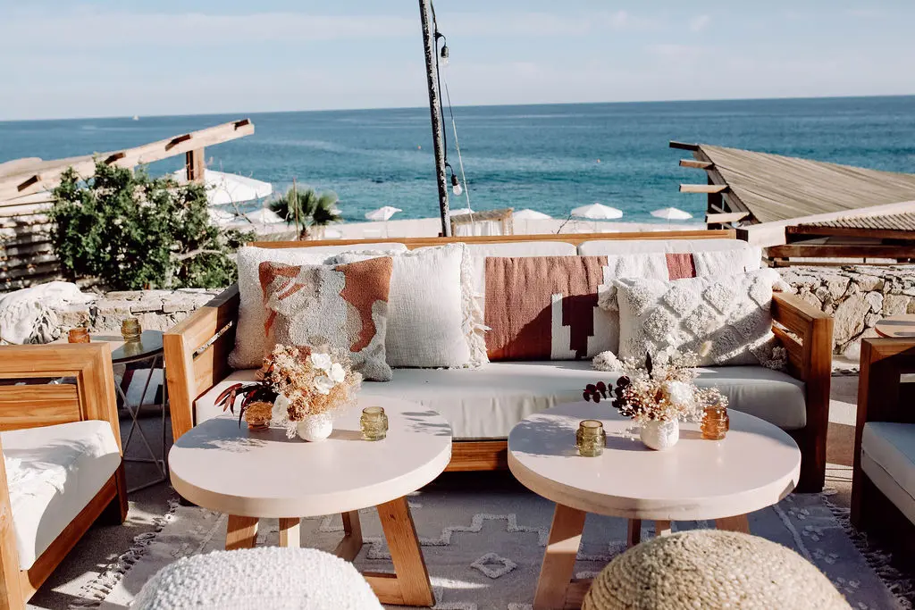 imagen de un sofá y dos pequeñas mesas redondas en una sala de estar abierta con vista al mar